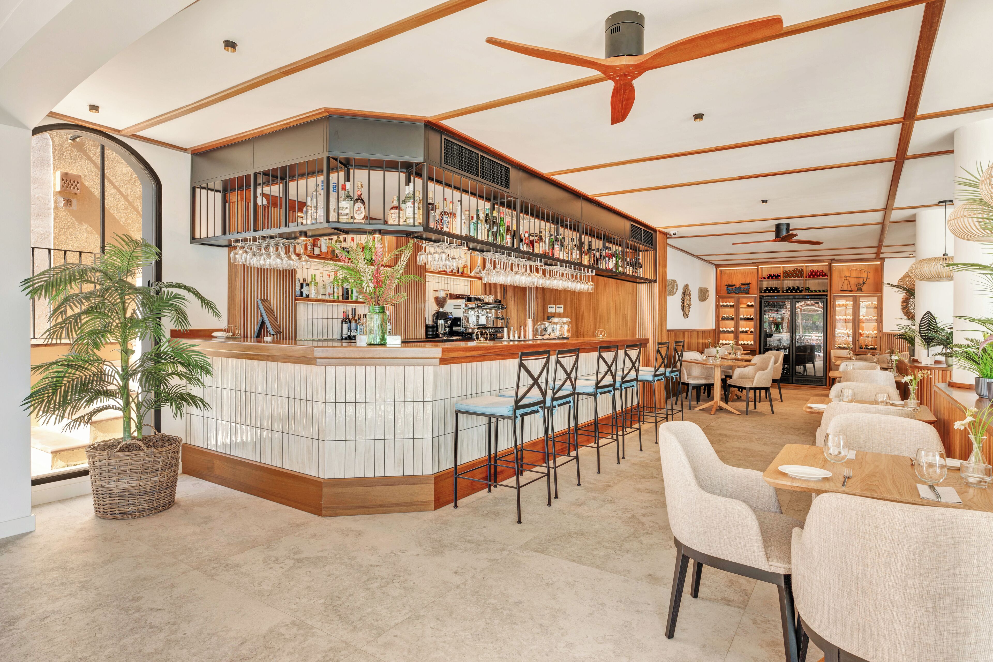 A modern bar area with a curved counter, bar stools, and a ceiling fan.