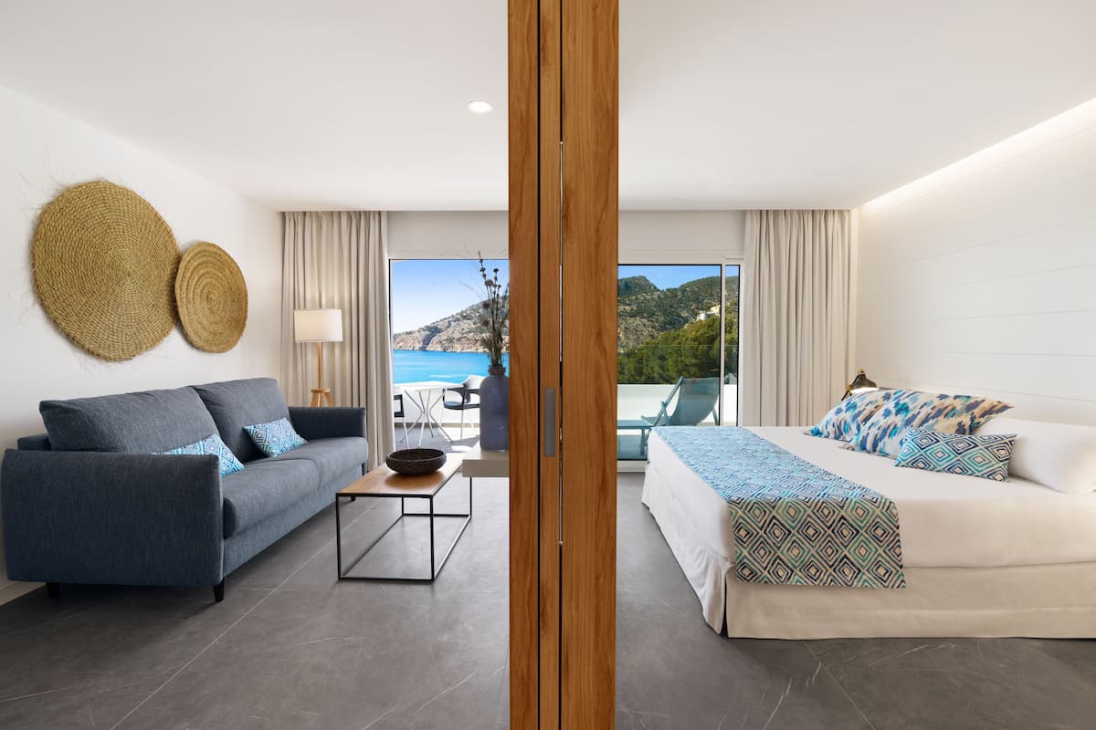 Een moderne hotelkamer met een bank, een bed, een tafeltje en uitzicht op zee.