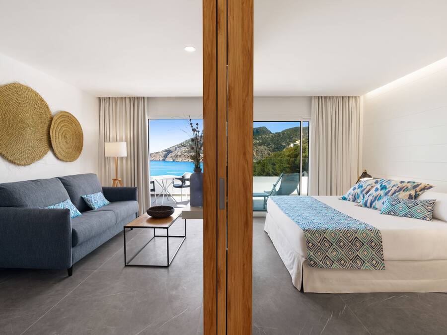 Habitación de hotel moderna con sofá, cama, una mesita y vista al mar.
