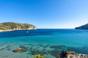 Un paysage côtier avec une eau turquoise cristalline, des rivages rocheux et un bateau à l’horizon.