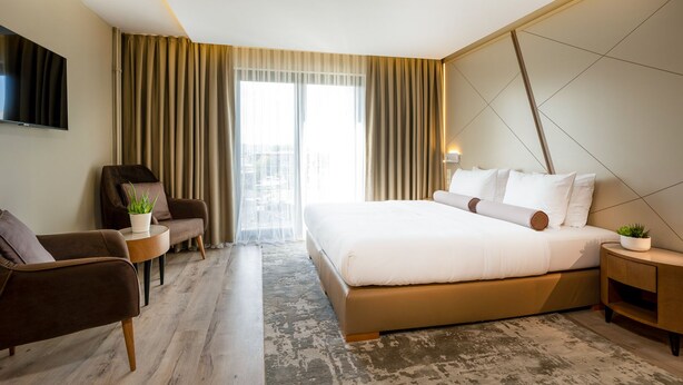 A hotel room with a large bed, a sofa, a TV, and a view of the city through the window. - Hotel Klassik Berlin (Berlin)