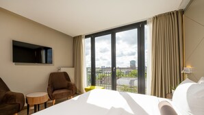 A hotel room with a large bed, two armchairs, a small round table, a flat-screen TV mounted on the wall, and a window with a city view. - Hotel Klassik Berlin (Berlin)