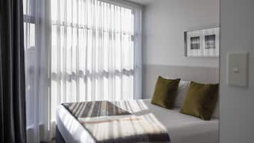 Habitación de hotel con una cama, una ventana con cortinas translúcidas, un cuadro enmarcado en la pared y un radiador.