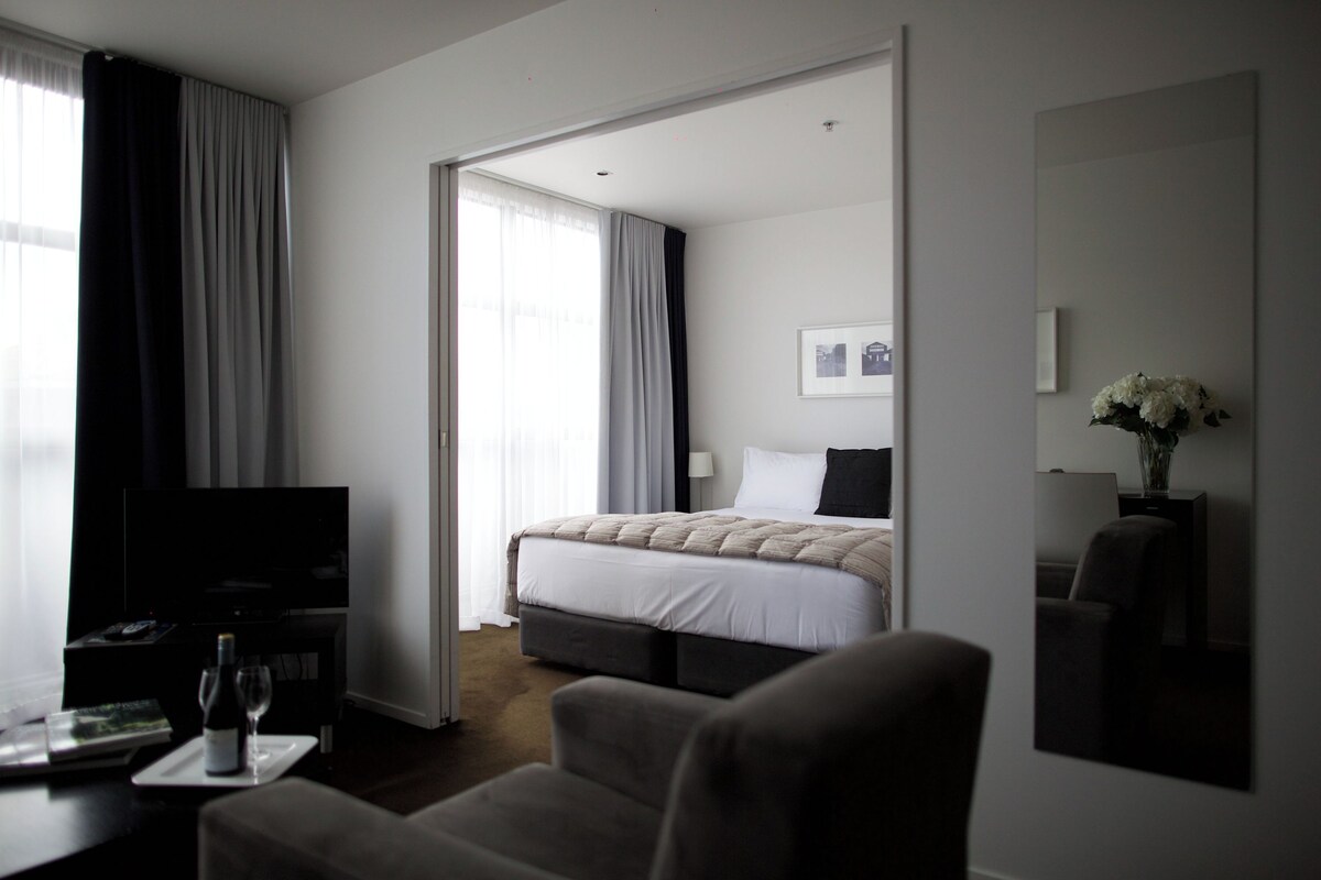 Ett hotellrum med en säng, en tv, ett skrivbord med ett vinglas och en spegel.