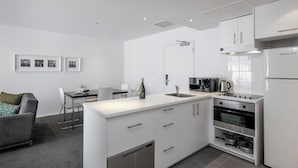 A modern kitchen with white cabinetry, a built-in oven, and a dining area with a gray sofa and a table. - Quest Parnell (Auckland)