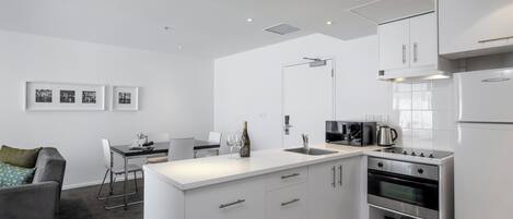 A modern kitchen with white cabinetry, a built-in oven, and a dining area with a gray sofa and a table.