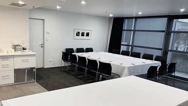 A modern conference room with a long table, chairs, a sink, and a window with curtains. - Quest Parnell (Auckland)