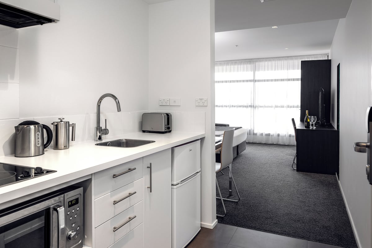 A modern kitchen with a built-in oven, a sink, and a toaster. There is a dining area with a table and chairs visible in the background.