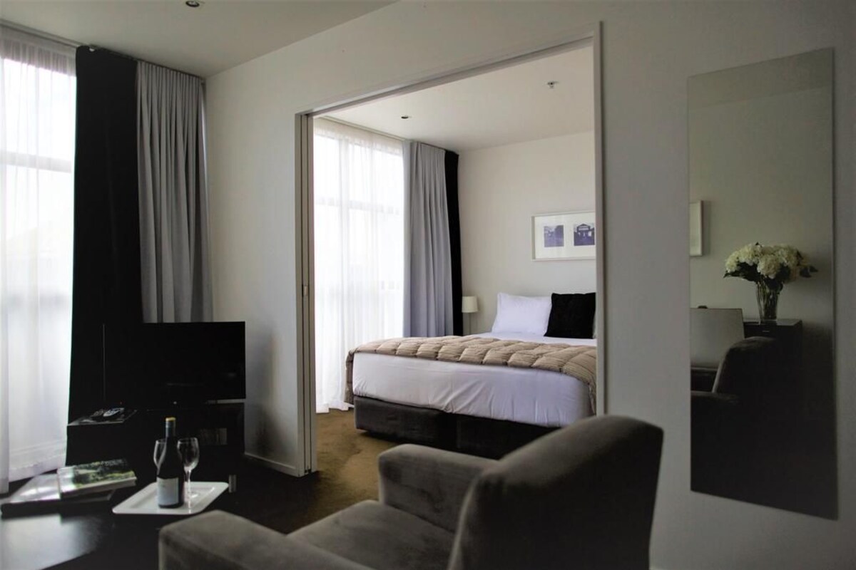 Ett hotellrum med en säng, en tv, en soffa och ett matbord med en flaska vin.