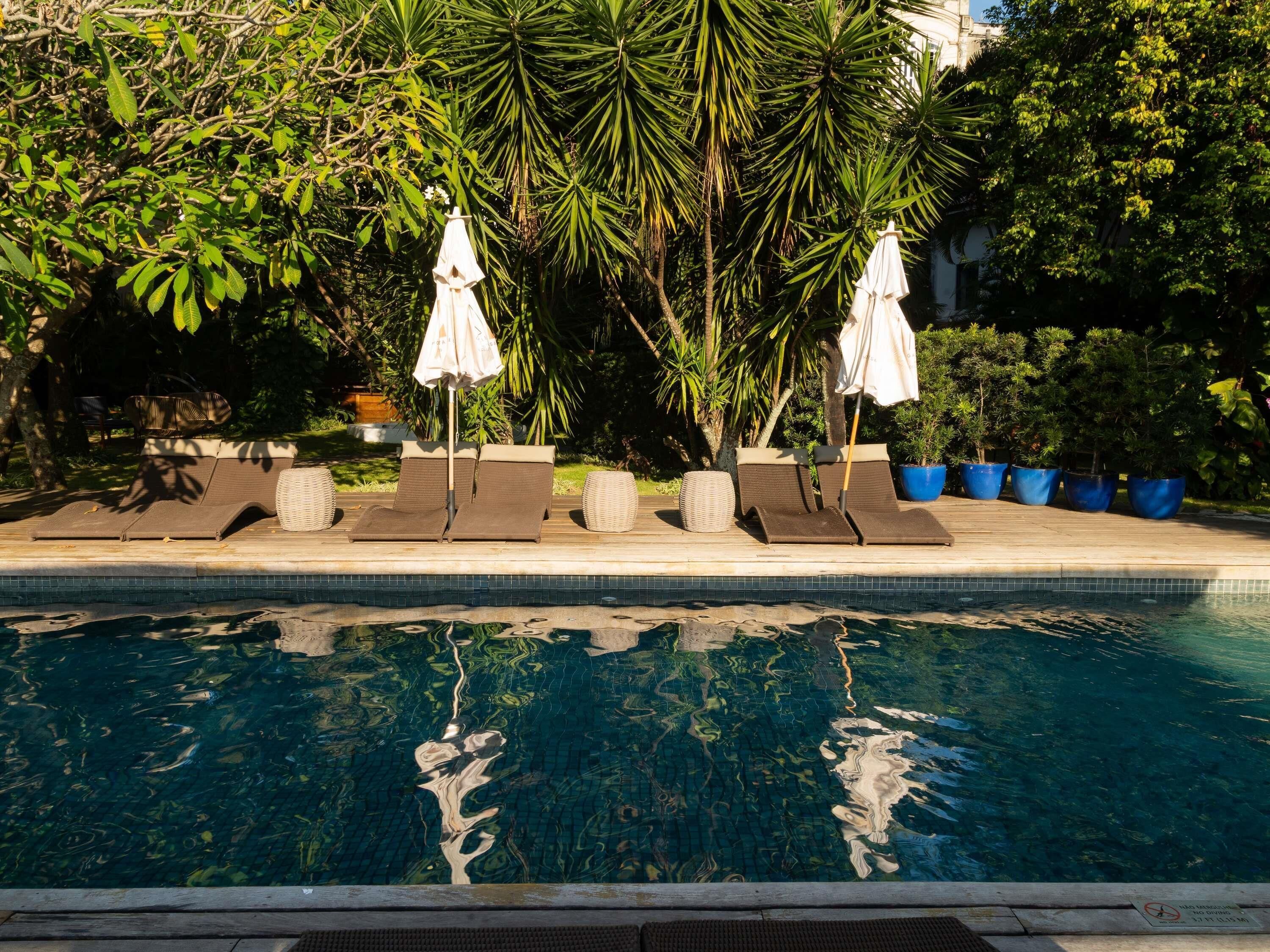 A poolside area with lounge chairs and umbrellas, surrounded by lush greenery and potted plants.