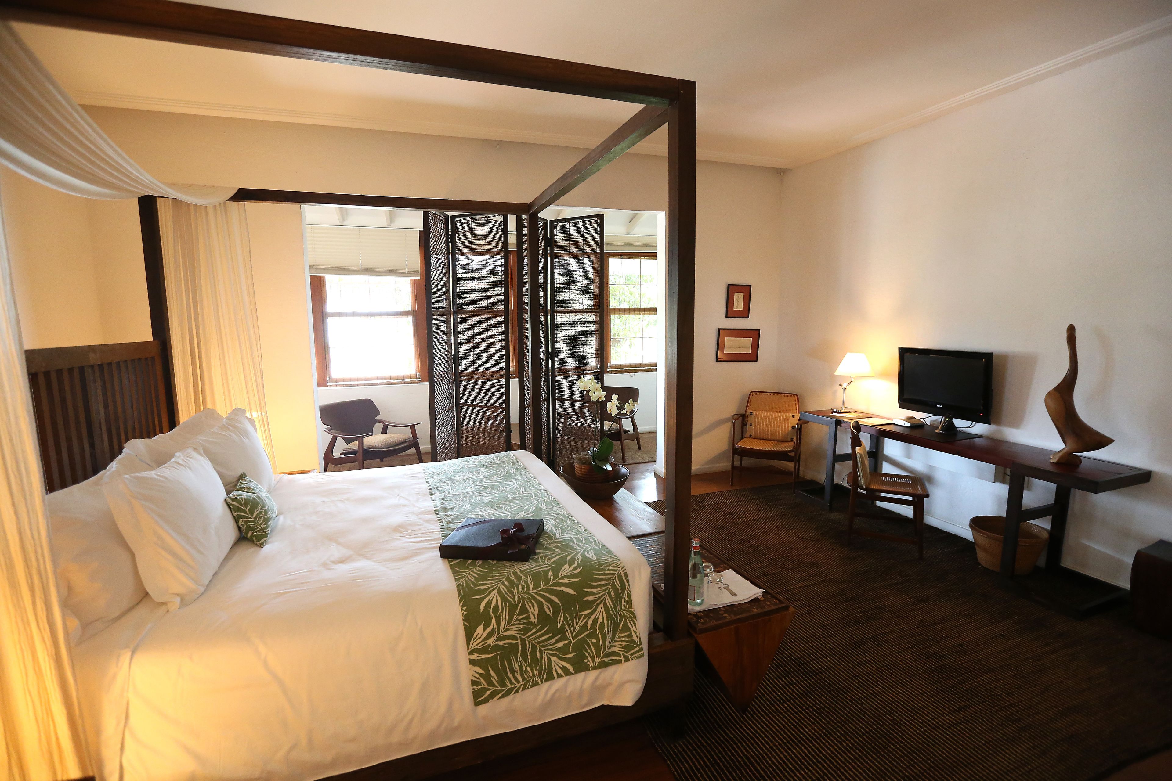A hotel room with a four-poster bed, a desk with a lamp, a television, and a chair.