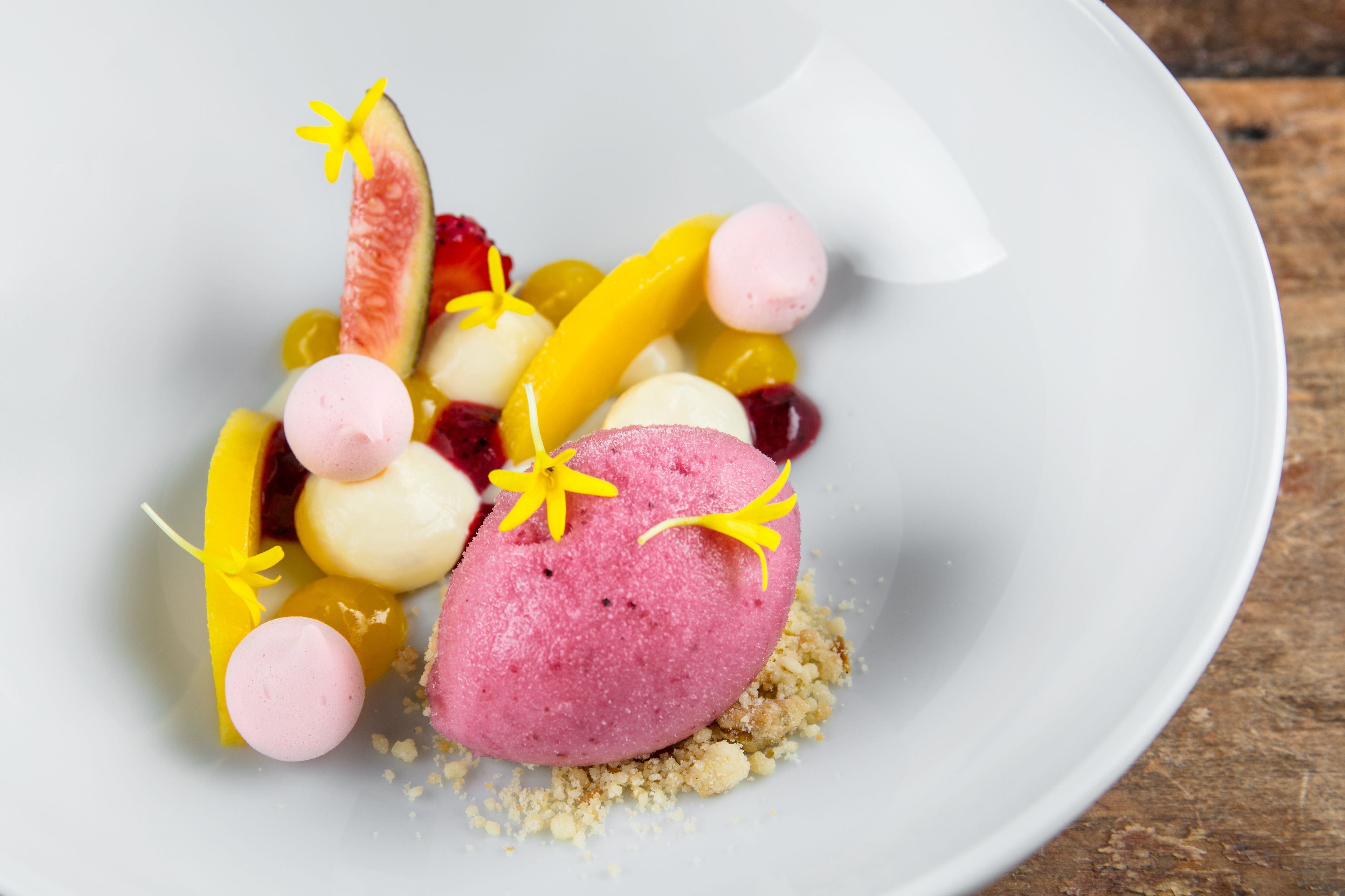 Un plato de postre con diversas frutas y una porción de helado rosa.