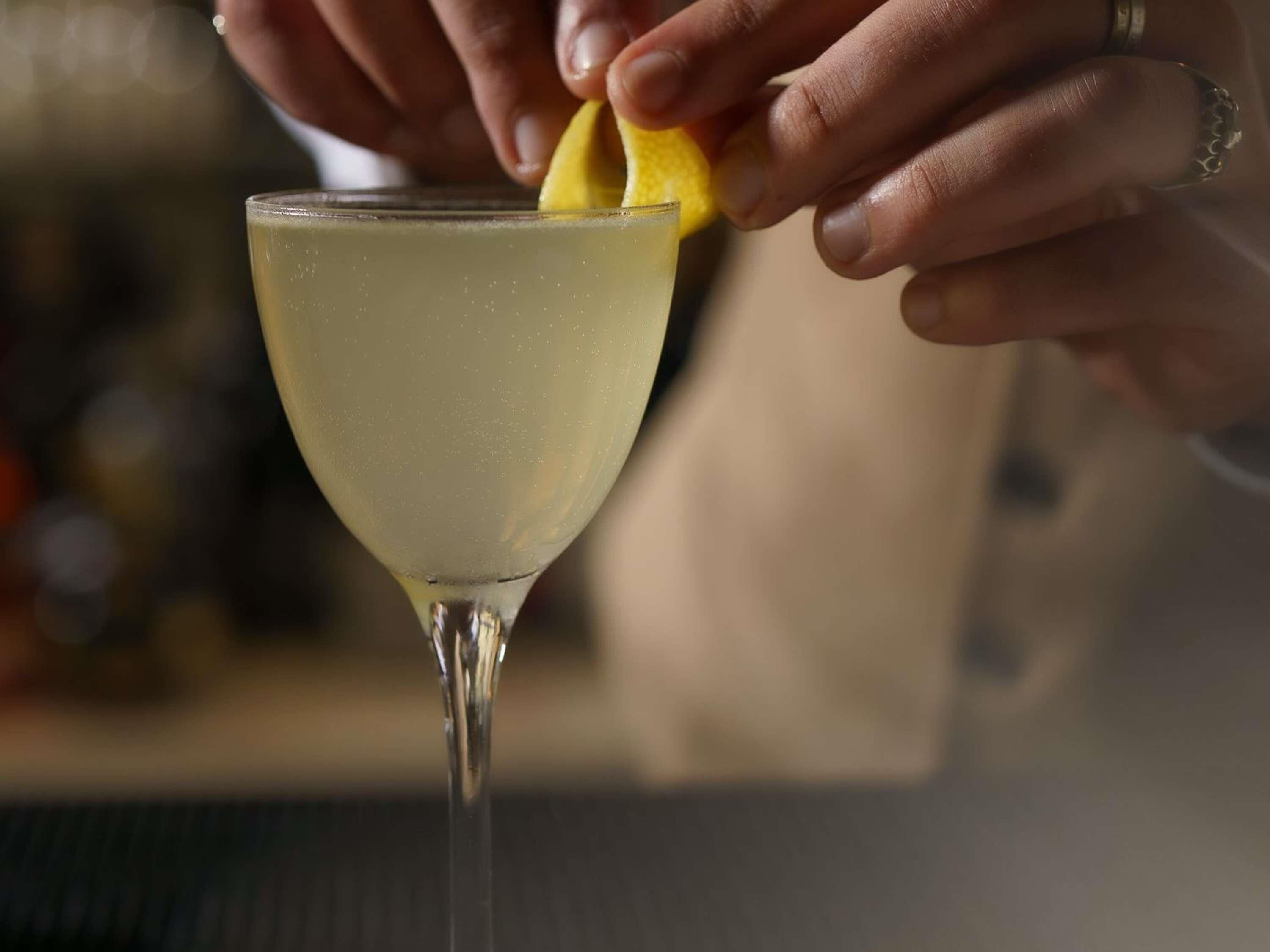 A person squeezing a lemon into a cocktail glass.