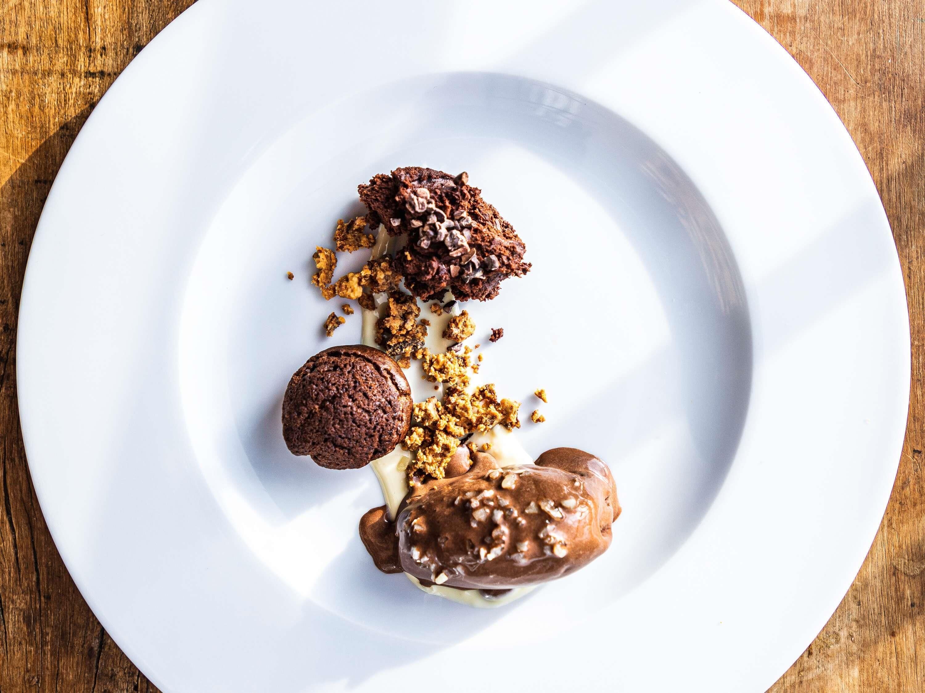 A white plate with three desserts on a wooden table.