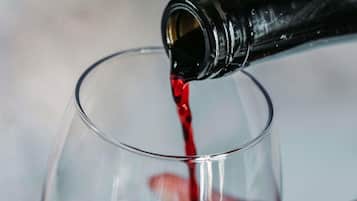 Une main verse un liquide rouge d’une bouteille dans un verre transparent.