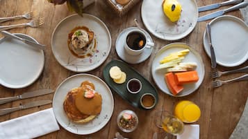 A breakfast setting with plates of pancakes, a croissant, and a variety of fruits and vegetables.