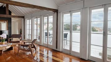 Une pièce spacieuse dotée d’un plancher en bois, de grandes portes-fenêtres coulissantes donnant sur une terrasse extérieure et d’un plafond avec des poutres en bois.
