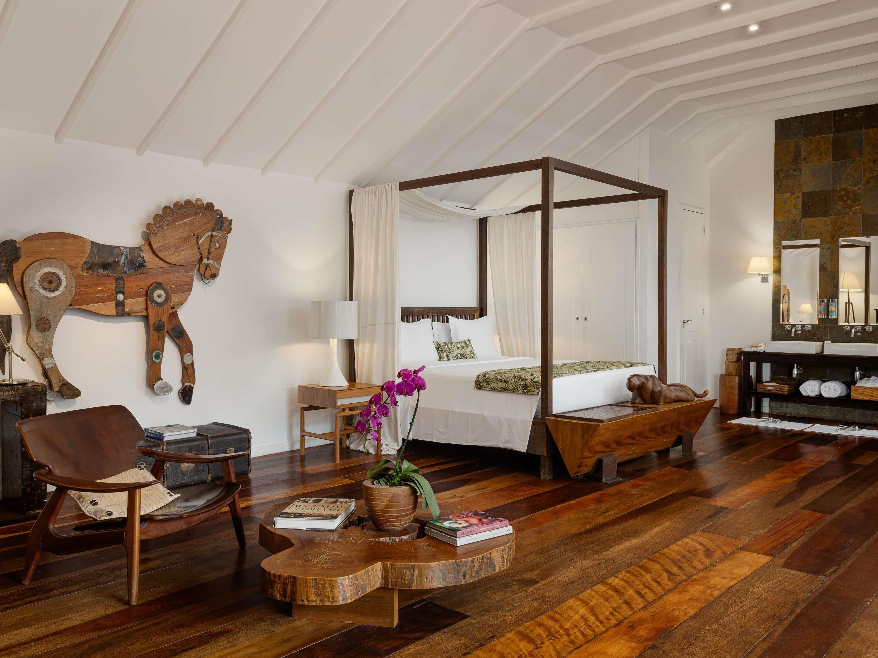 A spacious room with a four-poster bed, a wooden horse sculpture, a round wooden coffee table, and a large mirror.