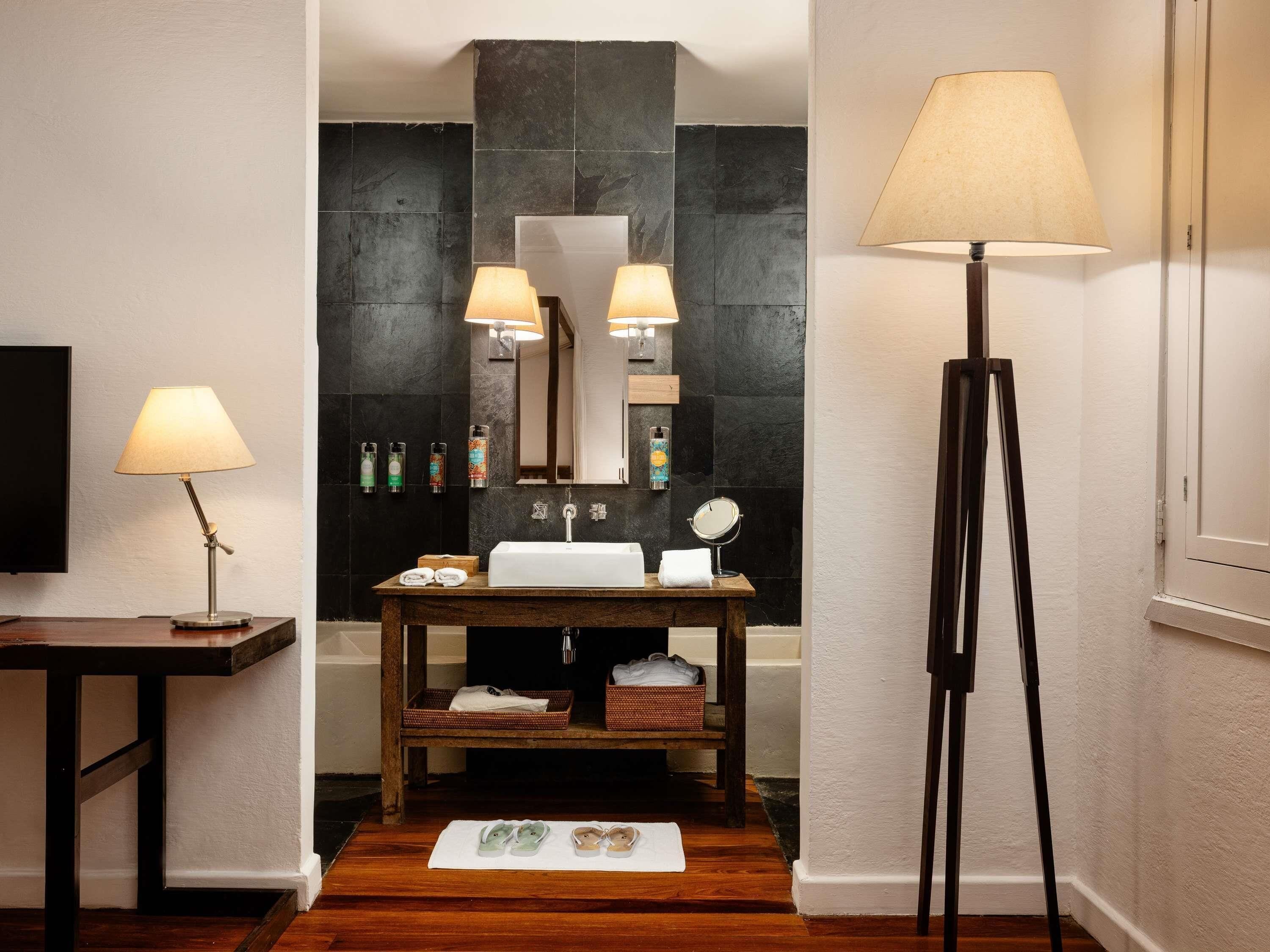 A bathroom with a wooden vanity, a large mirror, a floor lamp, and a bathtub.