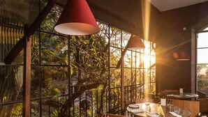 A restaurant with a view of lush greenery through large windows, wooden furniture, and red pendant lights. - Santa Teresa Hotel Rio de Janeiro - MGallery Collection (Rio de Janeiro)