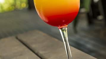A glass of layered drink with a red chili on the rim, placed on a wooden surface.