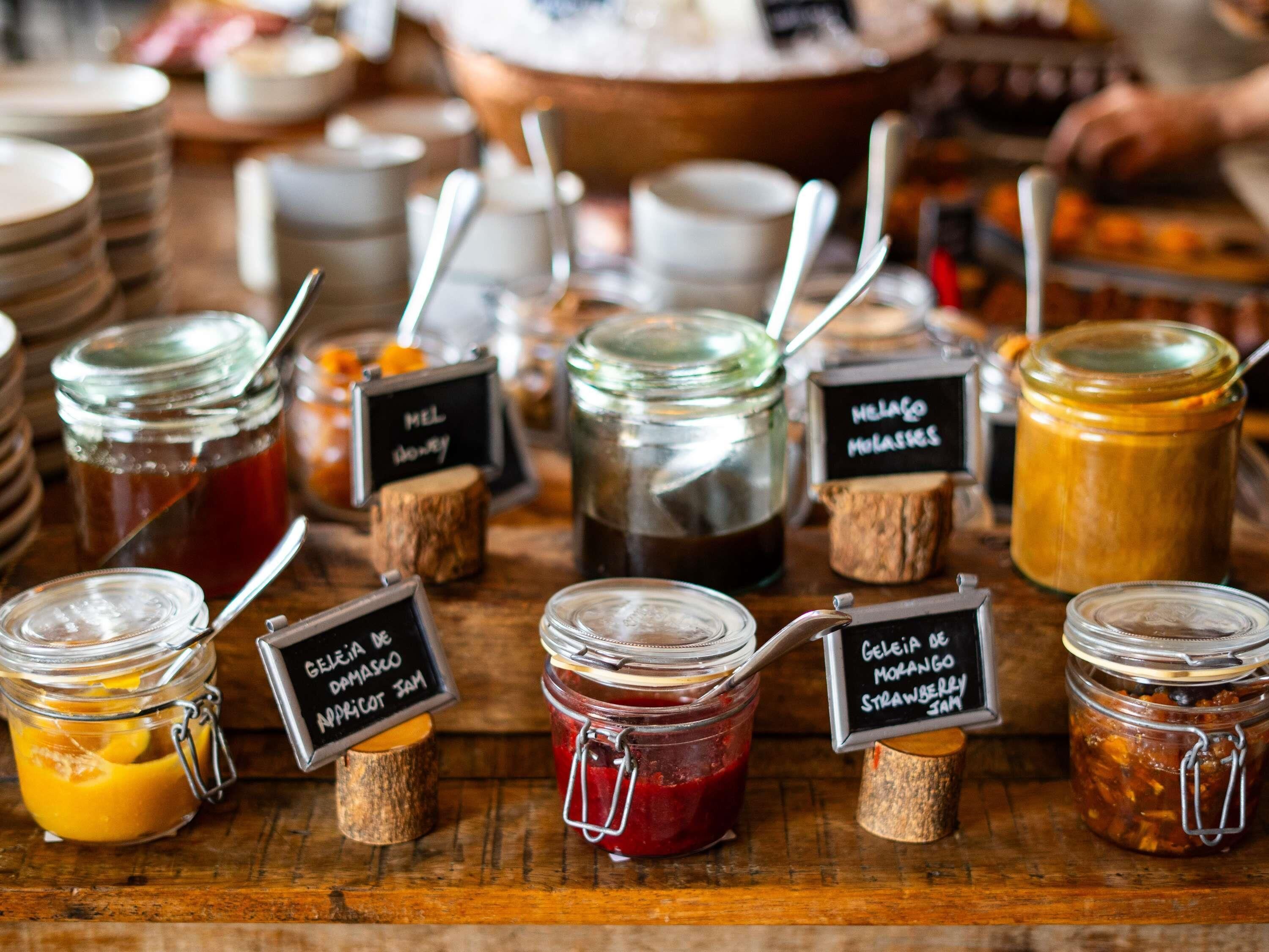 A variety of food items in jars with labels, arranged on a wooden surface.
