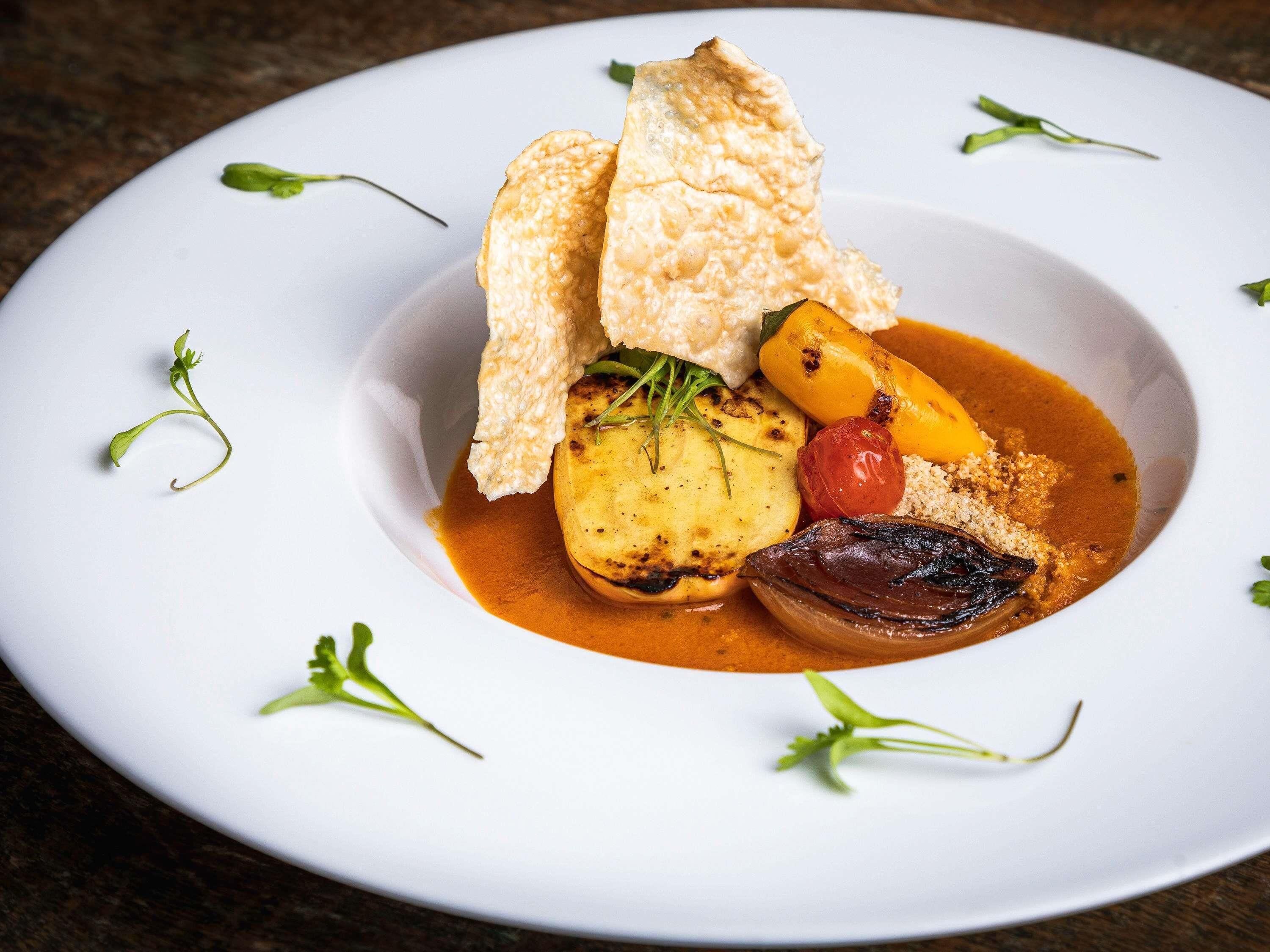 A white plate with a dish of food, including a grilled vegetable, a piece of meat, and a sauce.