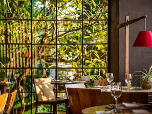 A restaurant with a wooden table and chairs, a red pendant light, and a view through a window with a grid pattern.