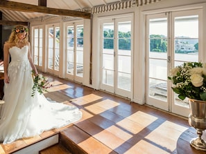 Eine Braut in einem weißen Hochzeitskleid hält einen Blumenstrauß, stehend in einem Raum mit großen Fenstern und einem Schachbrettfußboden.