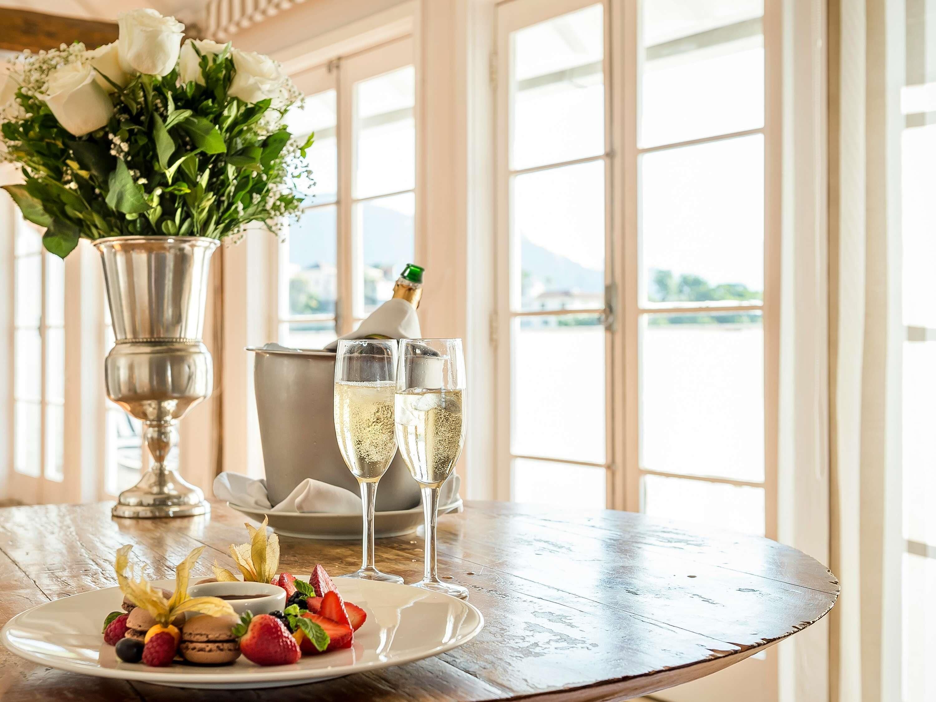 Een tafel met een bloemstuk, champagneglazen en een bord met macarons en fruit.