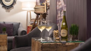 A cozy living room with a wooden coffee table, two wine glasses, a bottle of wine, a small plant, and a bookshelf in the background. - Hôtel Voltaire Opéra (Nantes)