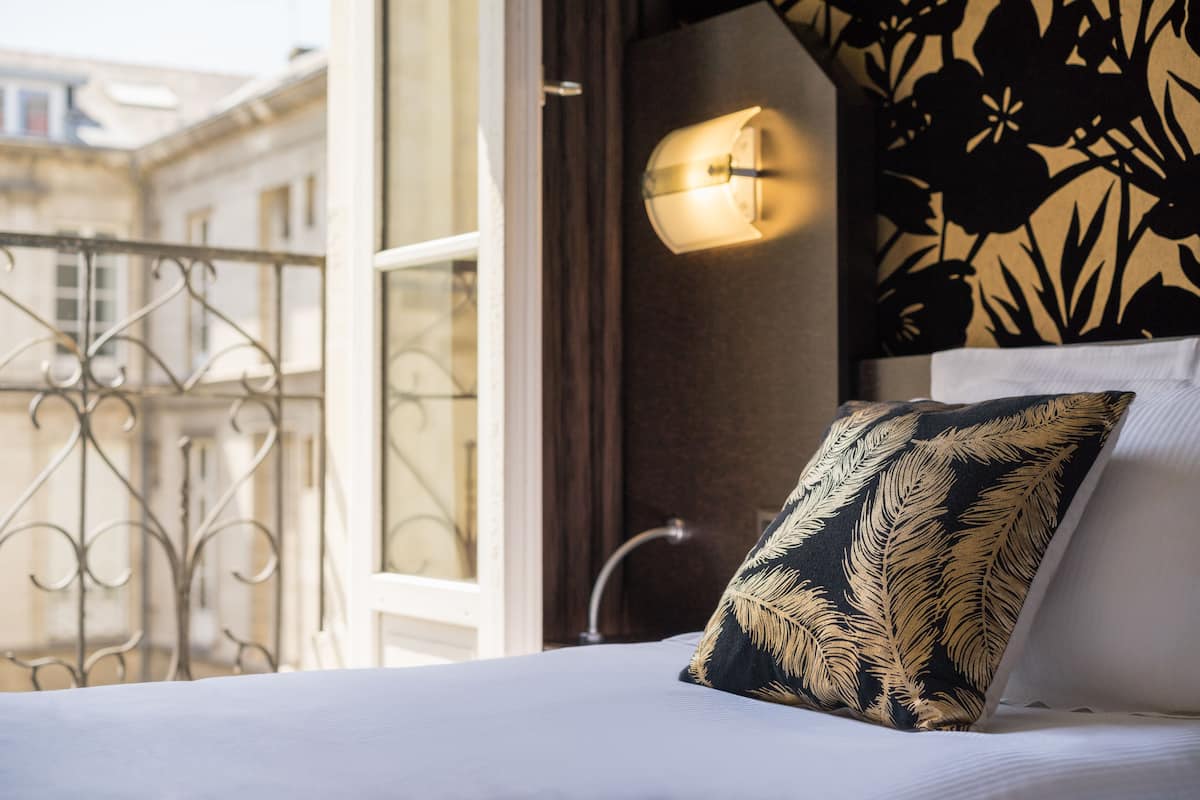Een hotelkamer met een bed, een raam met uitzicht op gebouwen, een muur met een bloemendesign en een wandlamp.