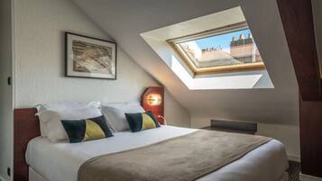 Slaapkamer met dakraam, een bed met kussens, een ingelijst schilderij aan de muur en een nachtkastje met een lamp.