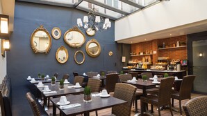 A restaurant with multiple dining tables and chairs, a chandelier, and a kitchen area visible through an open wall. - Hôtel Voltaire Opéra (Nantes)