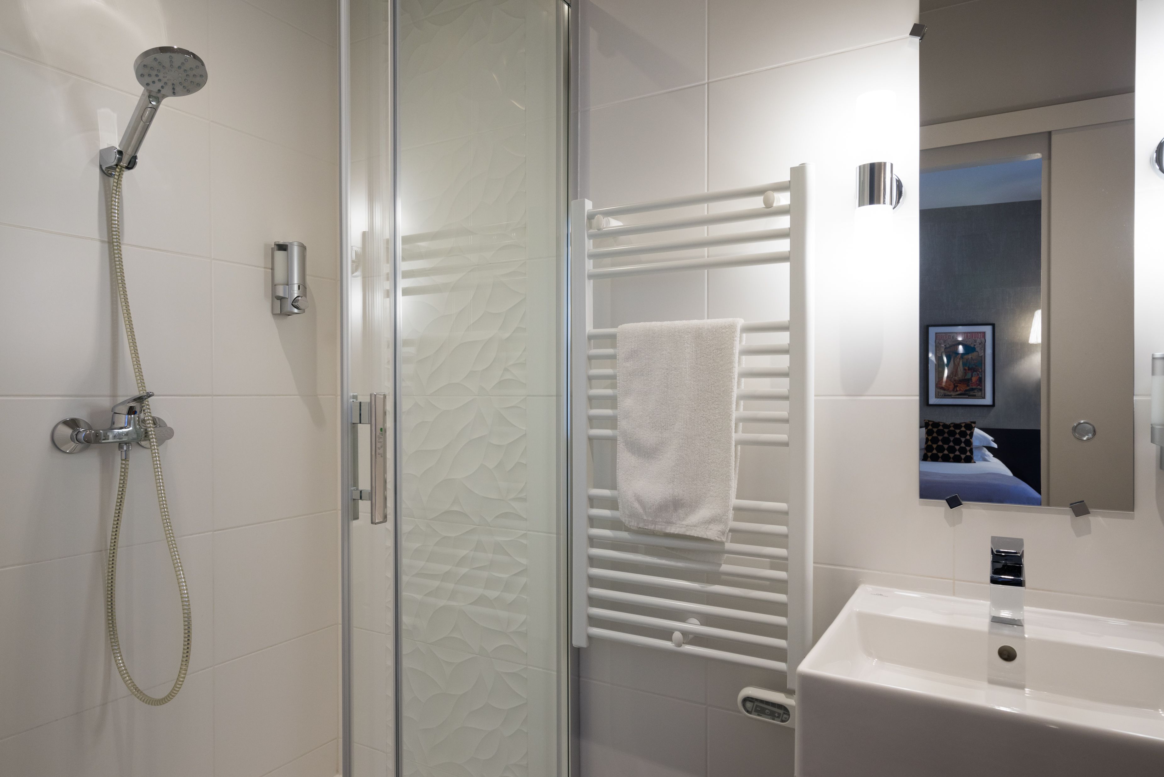 Un baño moderno con ducha envuelta en vidrio, un toallero blanco y un lavamanos con espejo superior.