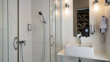 A modern bathroom with a glass-enclosed shower, a white sink, and a mirror with wall-mounted lights.