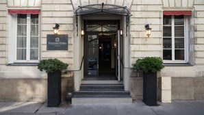 The entrance to Voltaire Opéra hotel with a stone facade, a red awning, and two potted plants. - Hôtel Voltaire Opéra (Nantes)