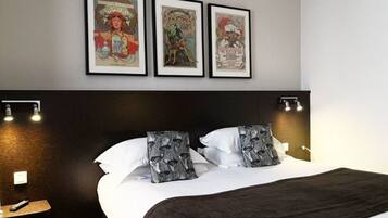 Een hotelkamer met een groot bed, twee ingelijste posters aan de muur en een nachtkastje met een lamp.