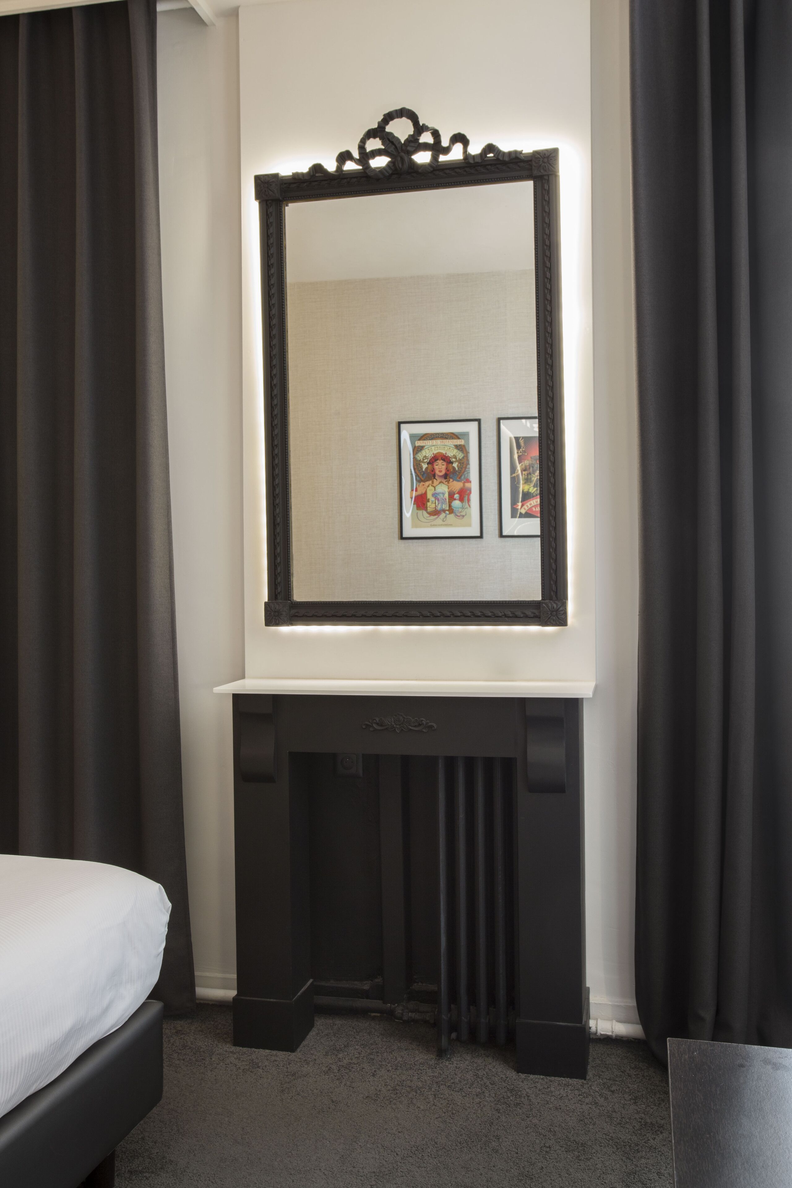 A room with a bed, a black console table, a large mirror, and two framed pictures on the wall.