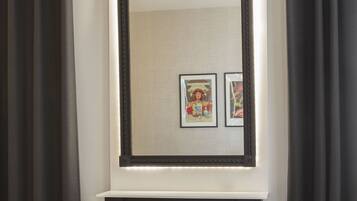 A room with a bed, a black console table, a large mirror, and two framed pictures on the wall.