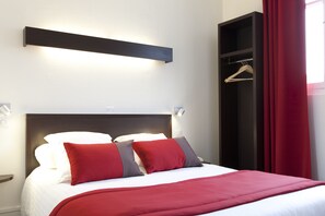 A neatly made bed with red and white bedding, a dark headboard, and a red curtain to the right.