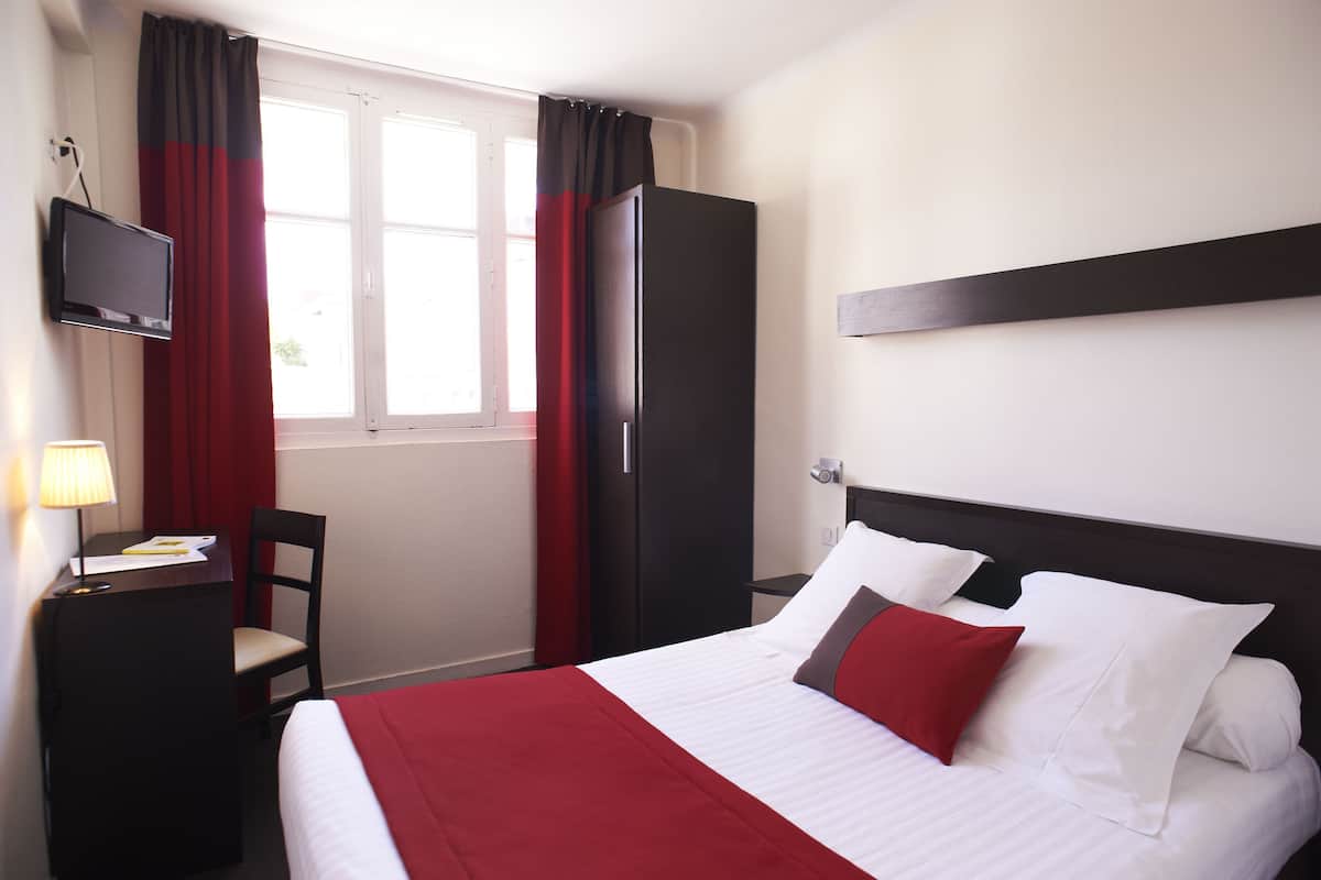 A hotel room with a bed, a desk, a chair, a TV, and a wardrobe.