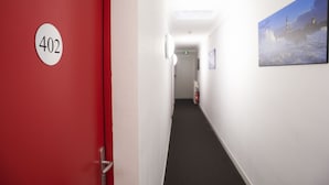 Un pasillo con una puerta roja con el número 402, paredes blancas y un cuadro de un faro a la derecha.