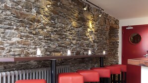 Una zona de bar con paredes de piedra, taburetes rojos y una puerta roja.