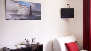 Habitación de hotel con escritorio, silla, cama con almohada roja, televisión montada en la pared y un cuadro de un faro.