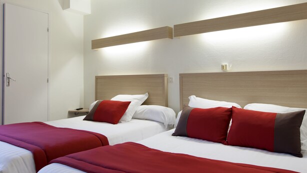 Una habitación de hotel con dos camas, cada una con ropa de cama roja y blanca, y cabeceros de madera.