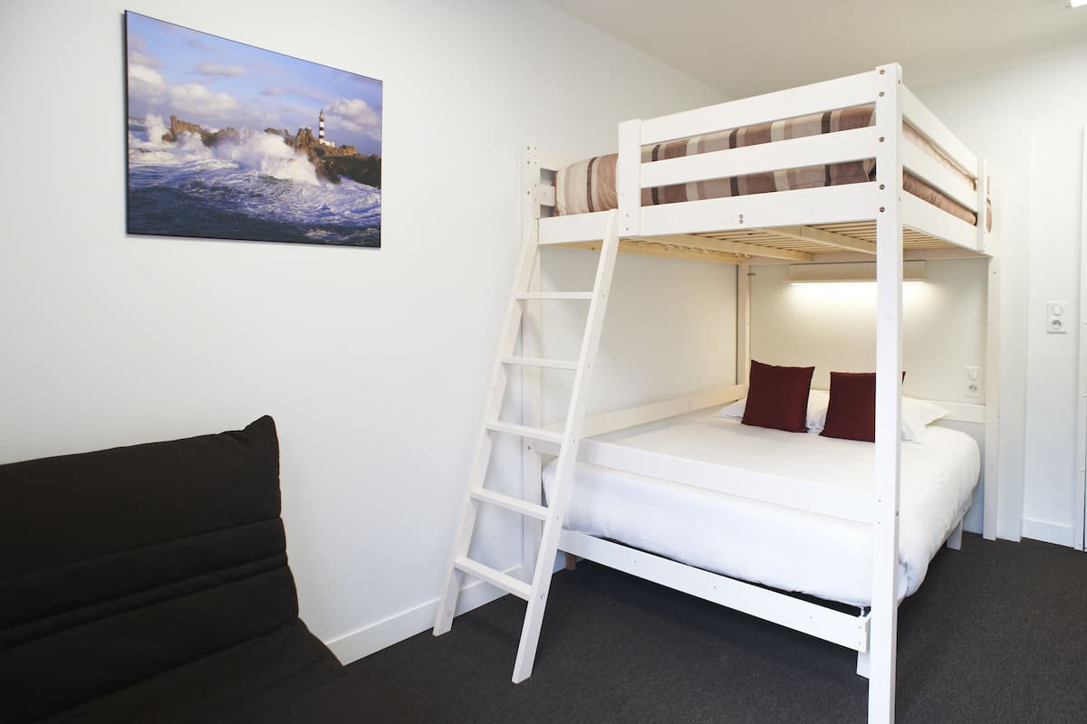 A bunk bed with a ladder, a black couch, and a painting of a lighthouse on the wall.