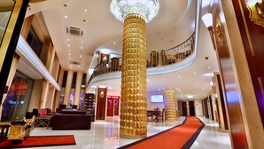 Un lobby espacioso con una columna dorada central, una alfombra roja y una escalera que conduce a un balcón.