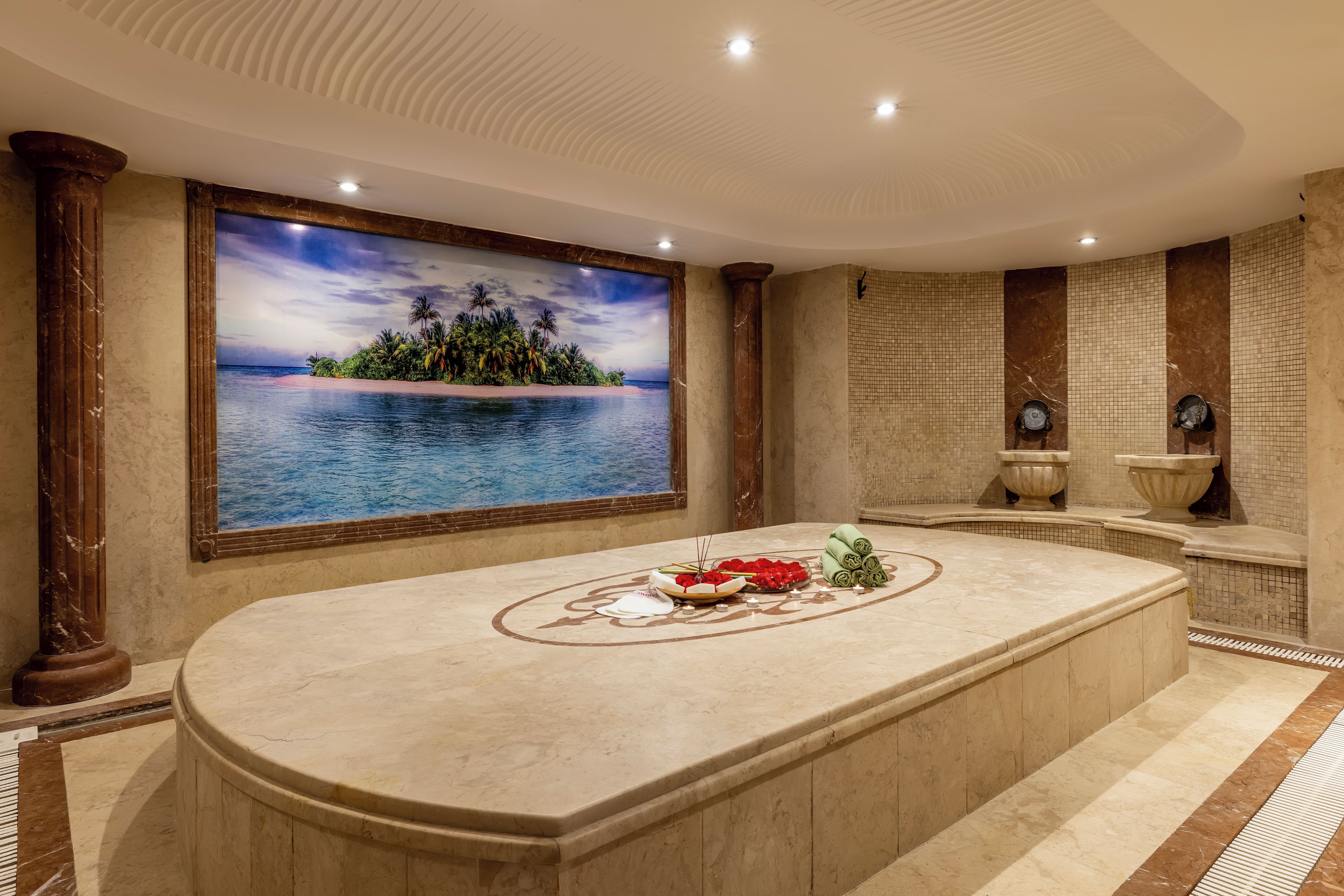 Un área de spa con una bañera grande, una isla decorativa con un mural tropical y un espacio de descanso con vistas al mar.
