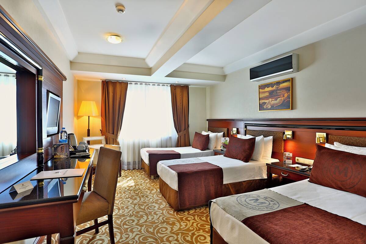 A hotel room with two beds, a desk, a chair, a TV, and a painting on the wall.